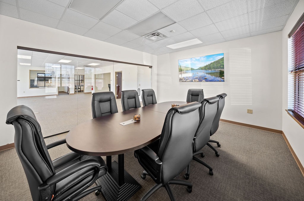 Conference room with an oval table, black leather chairs and a glass partition to open office space.