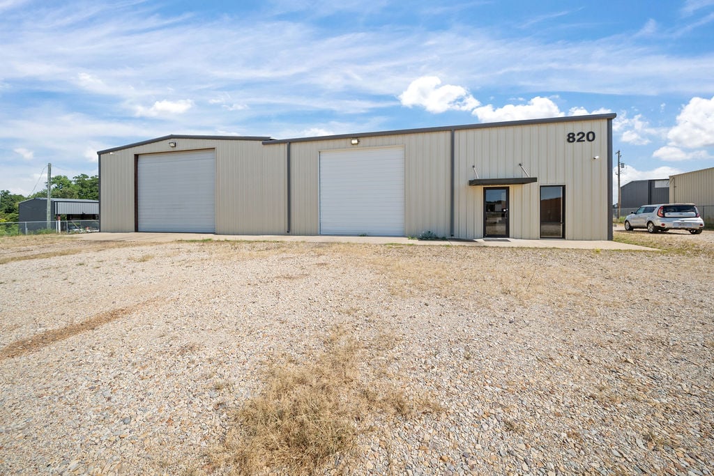 Metal warehouse building numbered 820 with grade-level overhead doors and a gravel service yard.