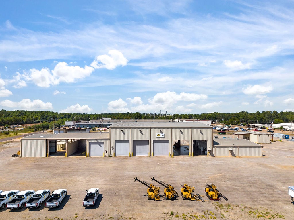 Elevated view of the main shop's overhead doors with a fleet of work trucks and drilling rigs parked in the yard.
