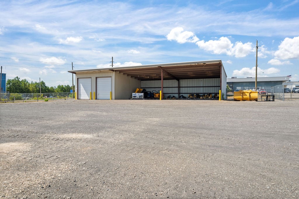 Covered equipment storage shed with two overhead doors and machinery parked under the open-sided canopy.