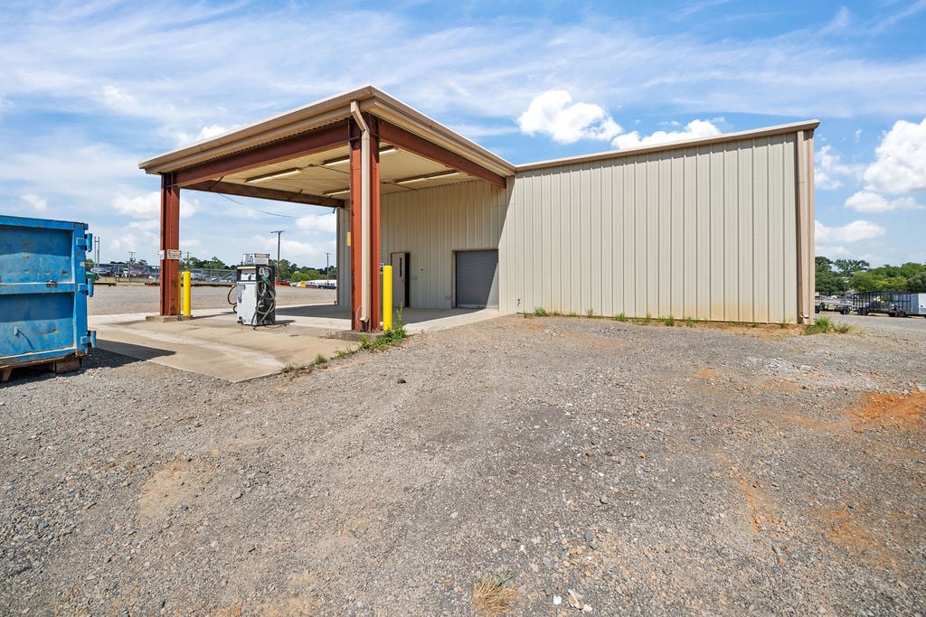 Metal building with a covered fuel and wash bay canopy and dispenser on a concrete pad.
