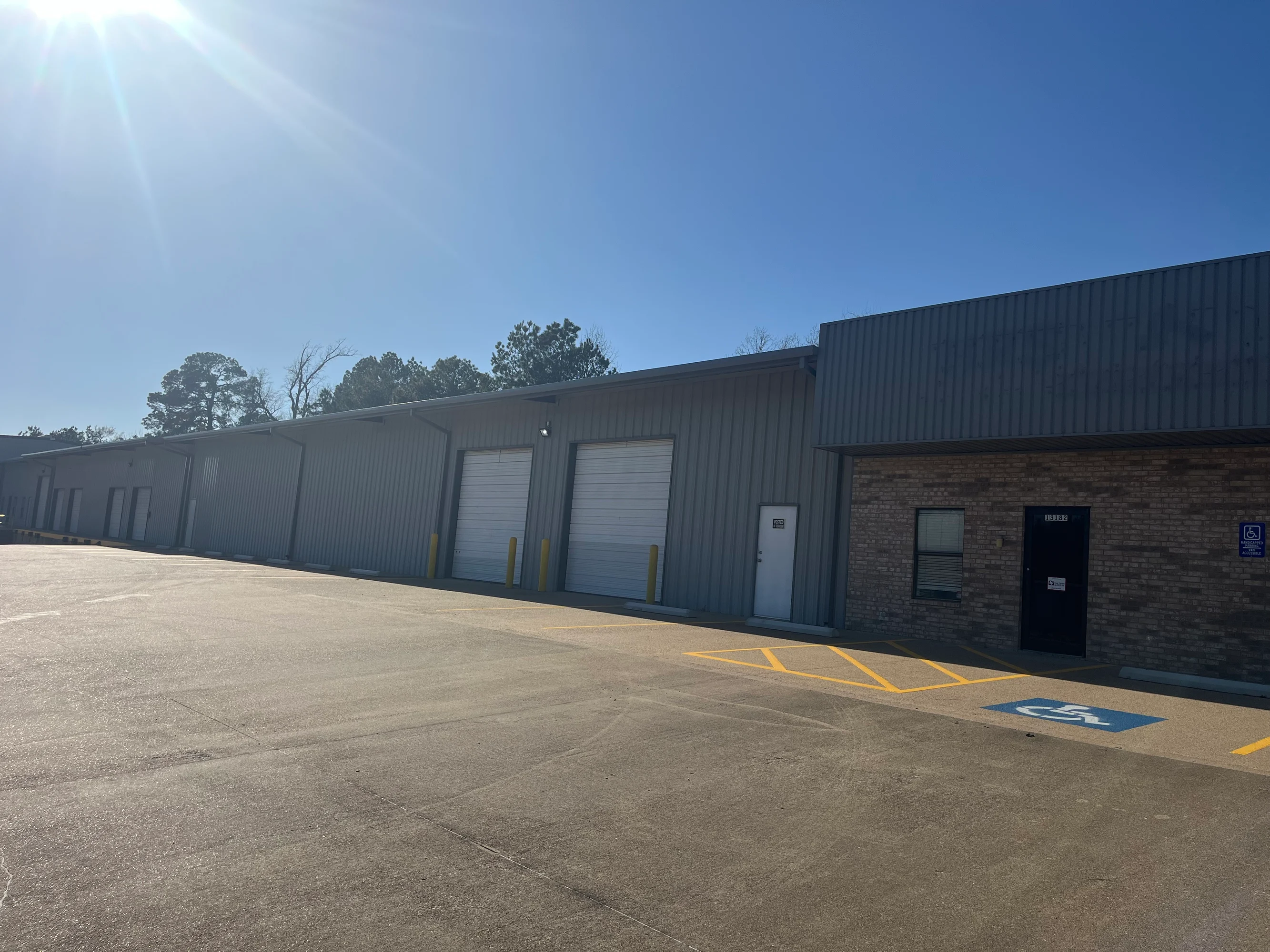 Exterior of the long gray metal warehouse with drive-in overhead doors and brick office entrance at Highway 110 Industrial in Tyler, Texas.