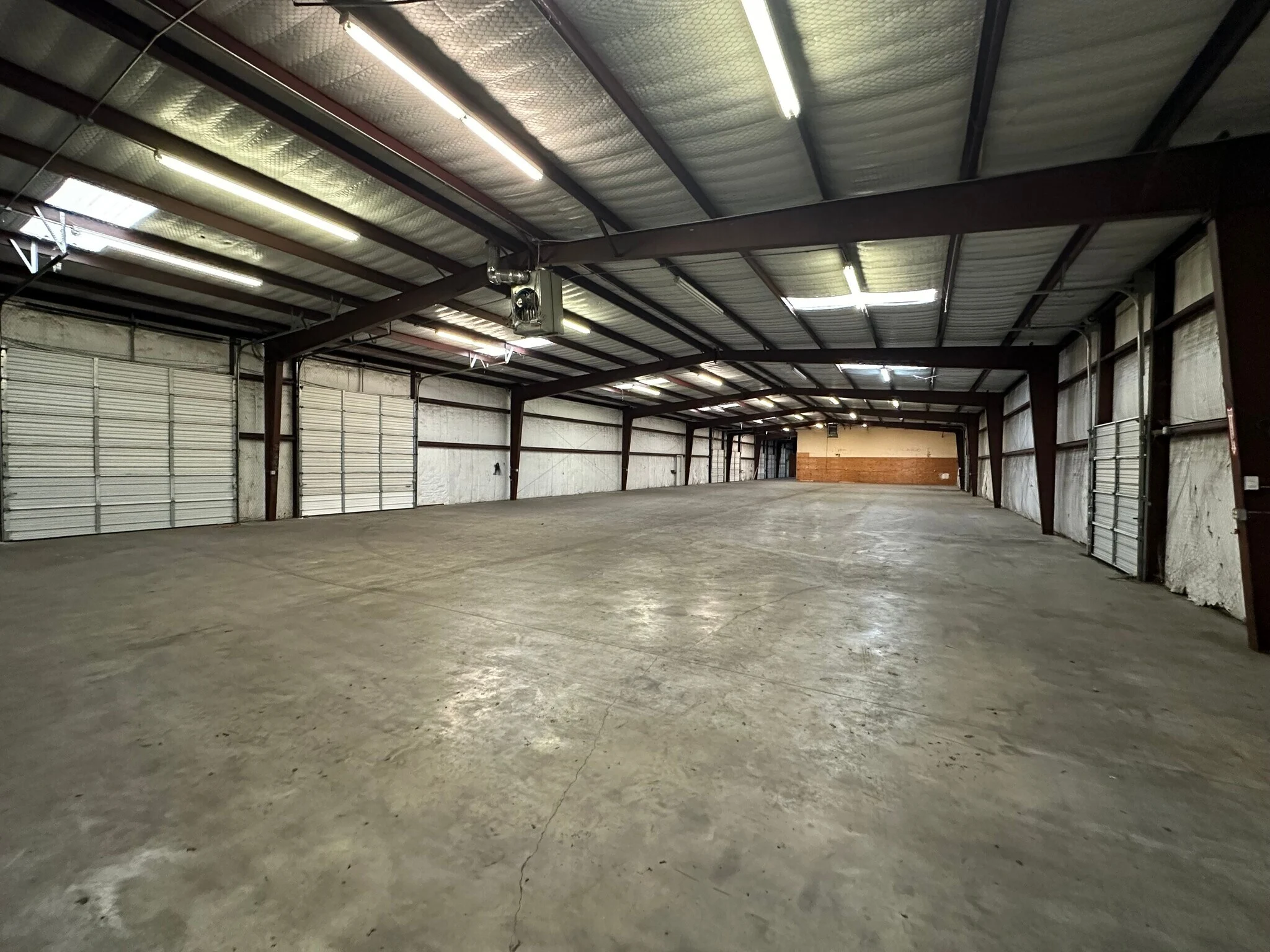 Empty warehouse interior with polished concrete floor and two white overhead doors at Highway 110 Industrial in Tyler, Texas.