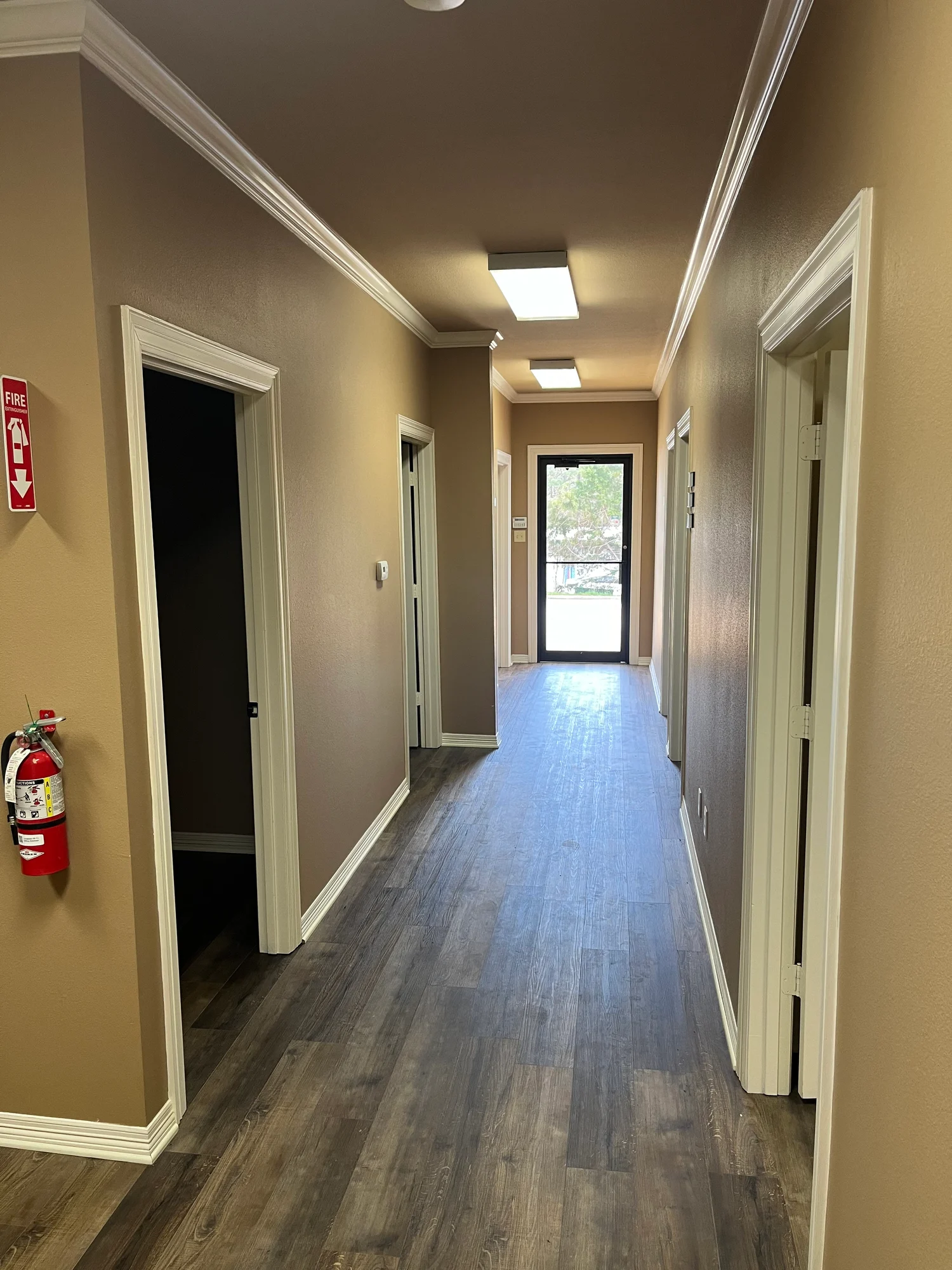 Office hallway lined with doors, fire extinguisher, and glass exterior door at the end at 13186 TX-110 in Tyler, Texas.