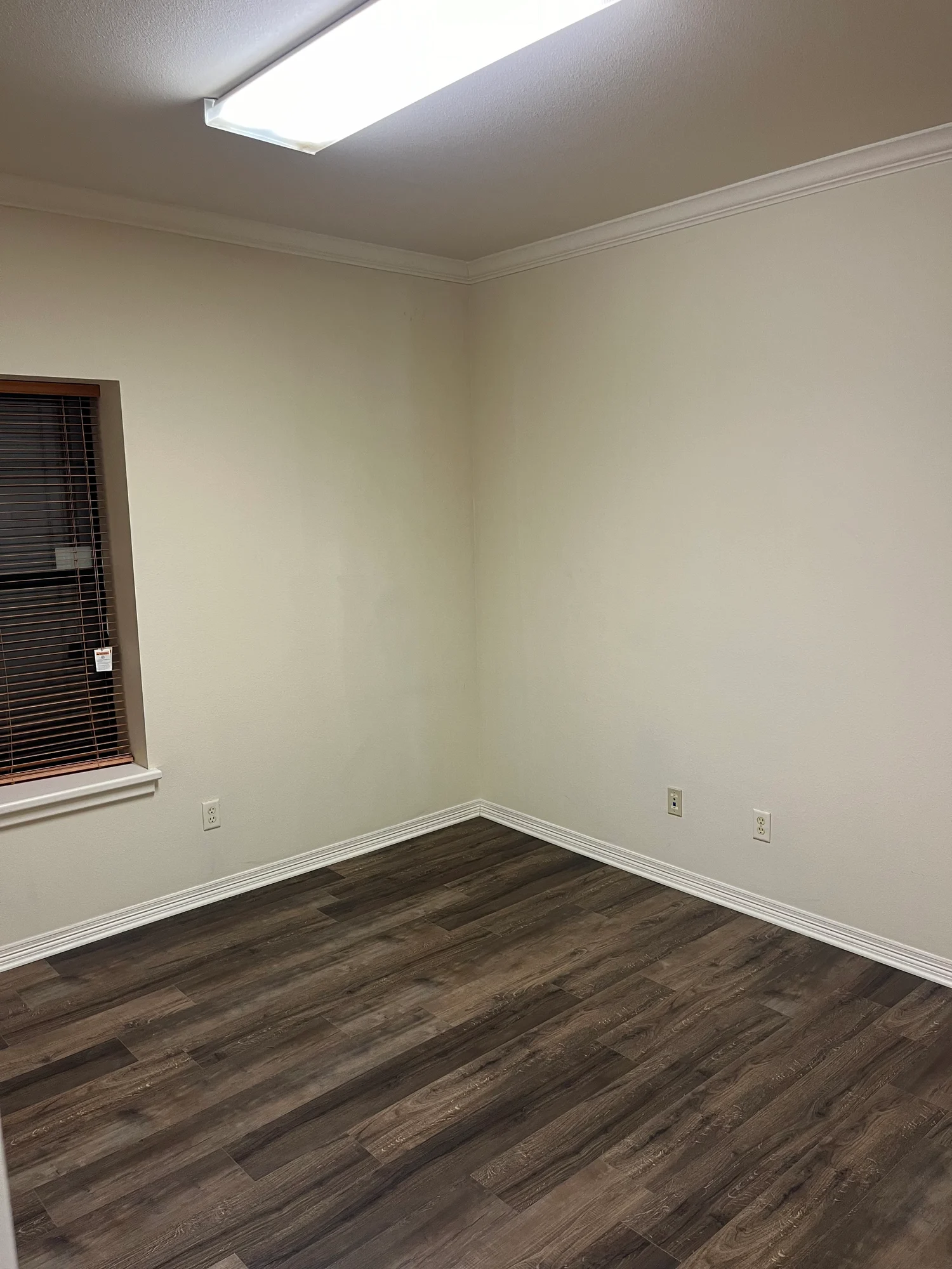 Empty private office with window blinds, crown molding, and wood-look flooring at Highway 110 Industrial in Tyler, Texas.
