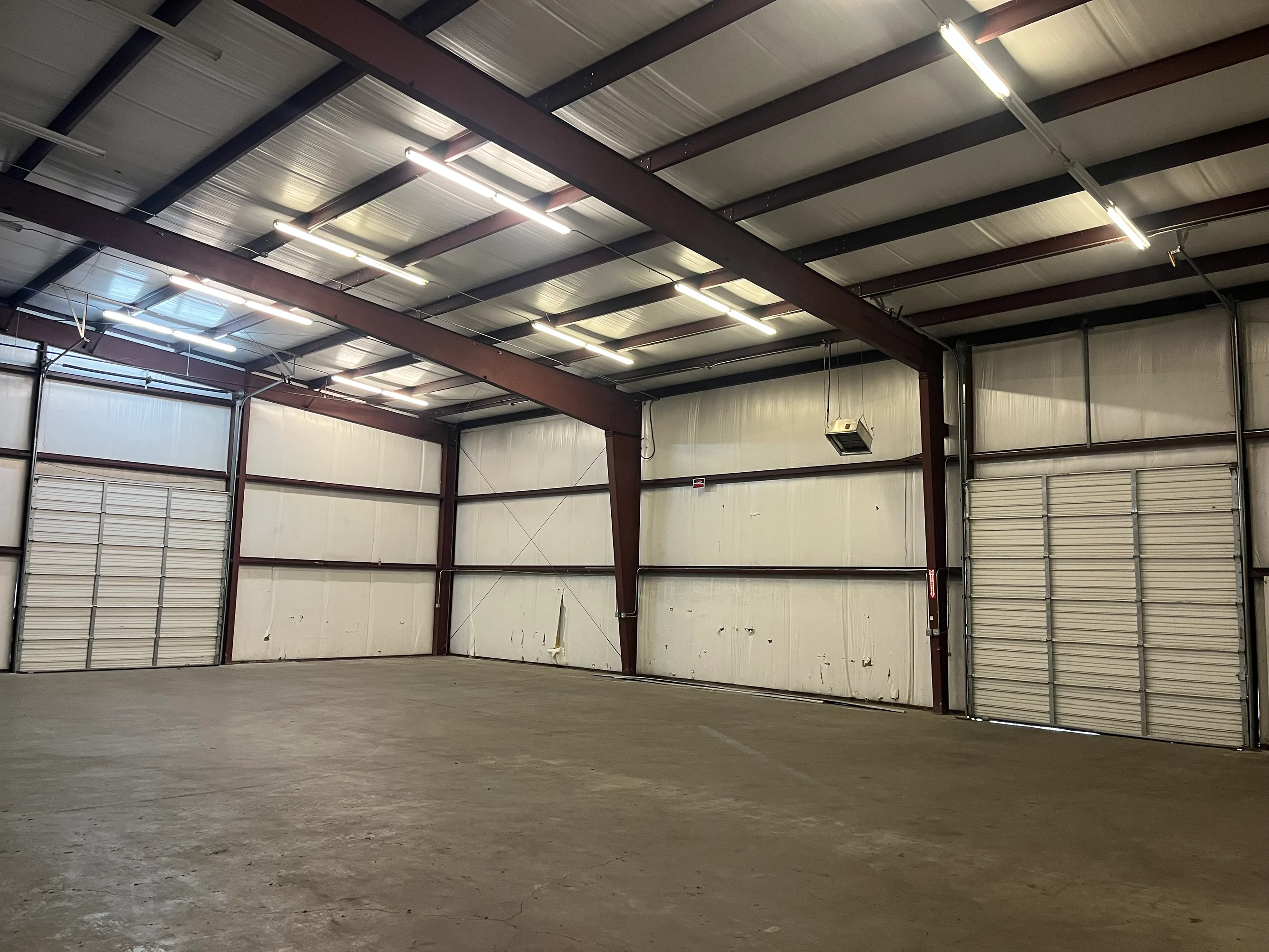 Warehouse interior flanked by two overhead roll-up doors under exposed steel trusses at Highway 110 Industrial in Tyler, Texas.